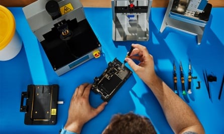 A person disassembling an iPhone on a blue antistatic mat.