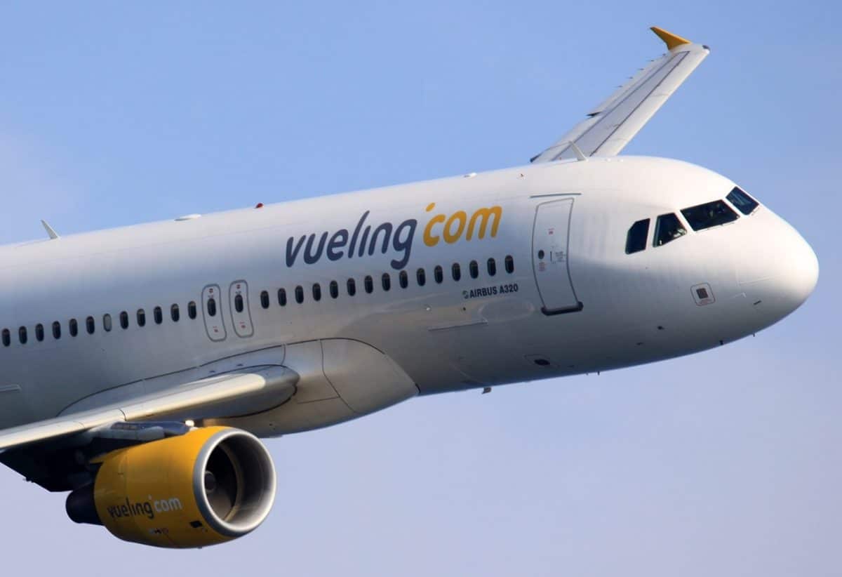 A plane is seen flying through the blue skies in support of Vueling Crypto payments.