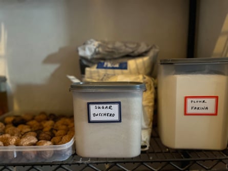 A pantry shelf containing a tray of nuts and clear plastic containers containing sugar and flour.