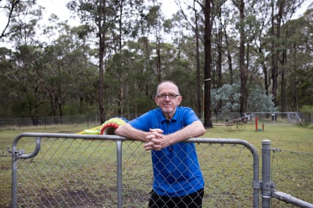 A man in a blue shirt leaning against an iron fence in a large suburban backyard.