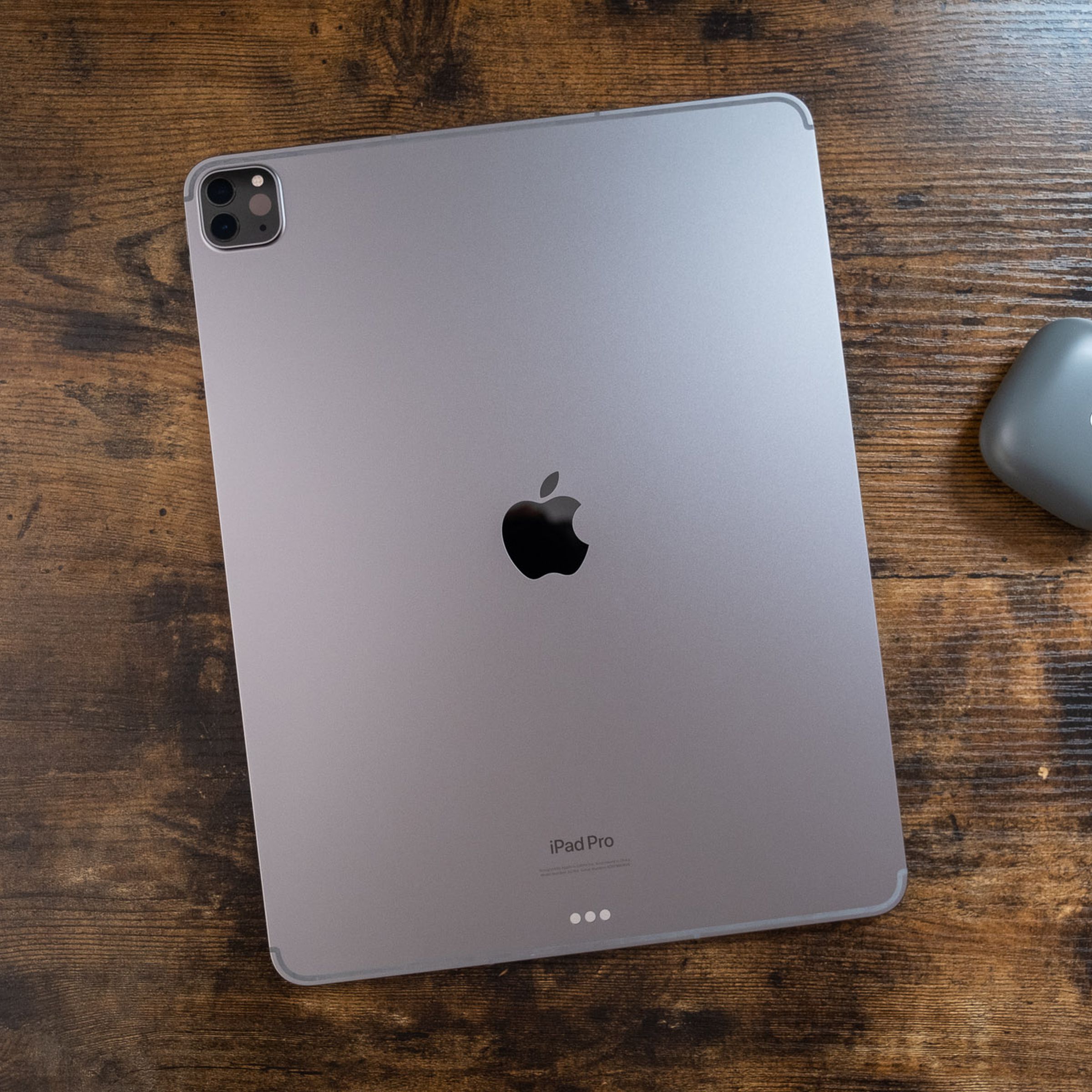 A space gray 12.9-inch iPad Pro face down on a wooden table, viewed from the top down.