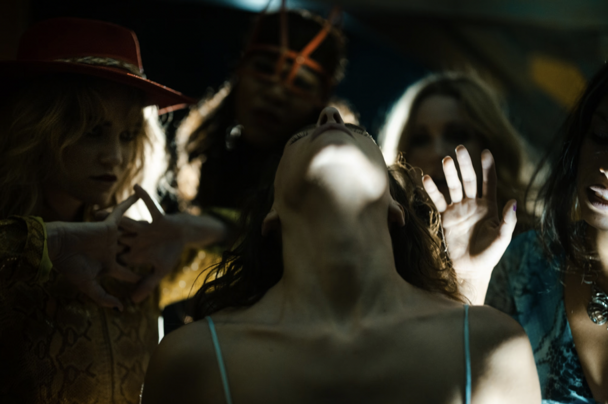 A group of women in a gloomy setting with their hands and heads tilted up and back.