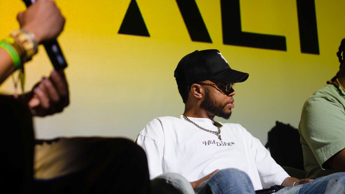 Artist Terrell Jones sits onstage during a panel, wearing a black cap and white shirt.