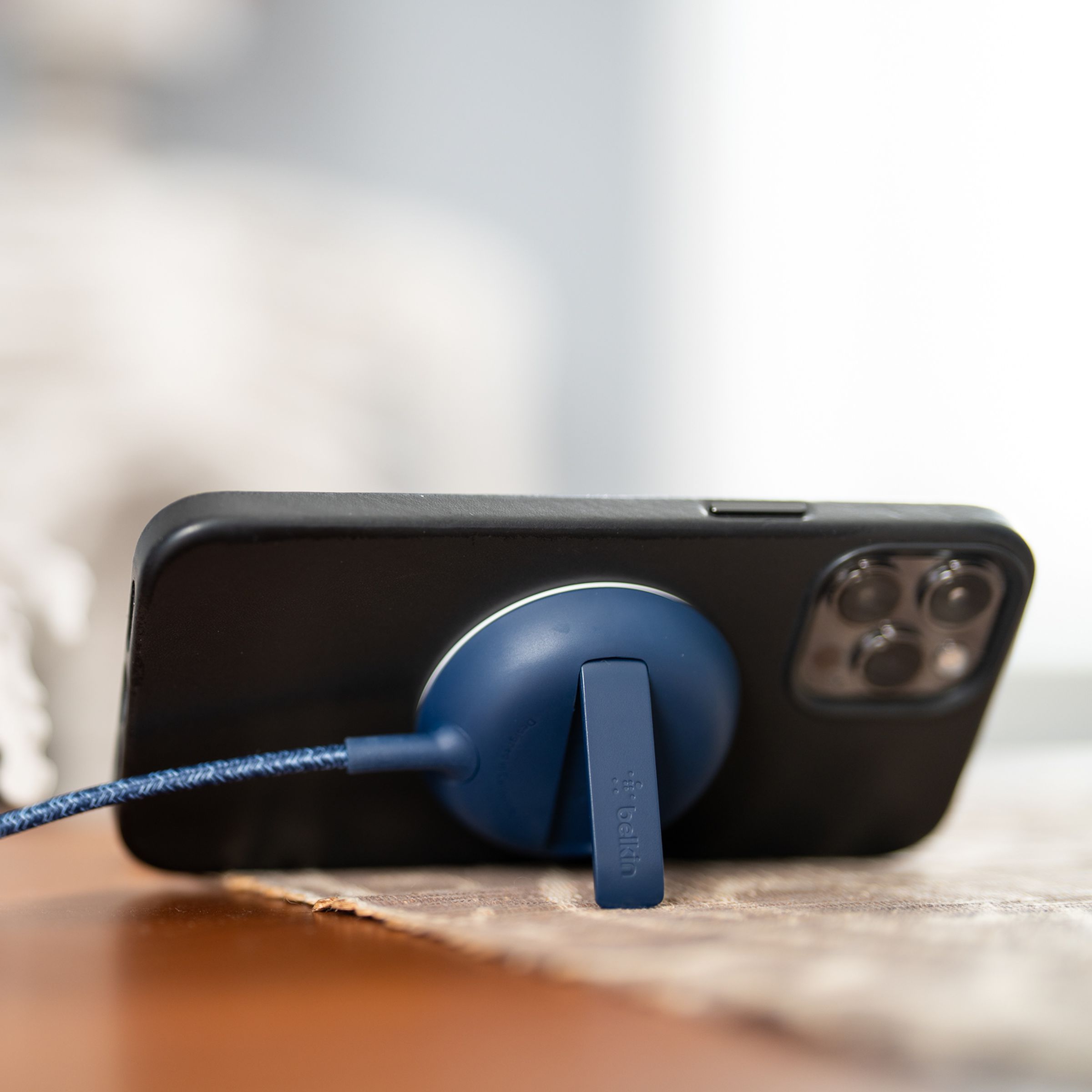 An iPhone held horizontally by a Belkin MagSafe charger holder on a table with a skeleton sitting in a chair looking at the phone.