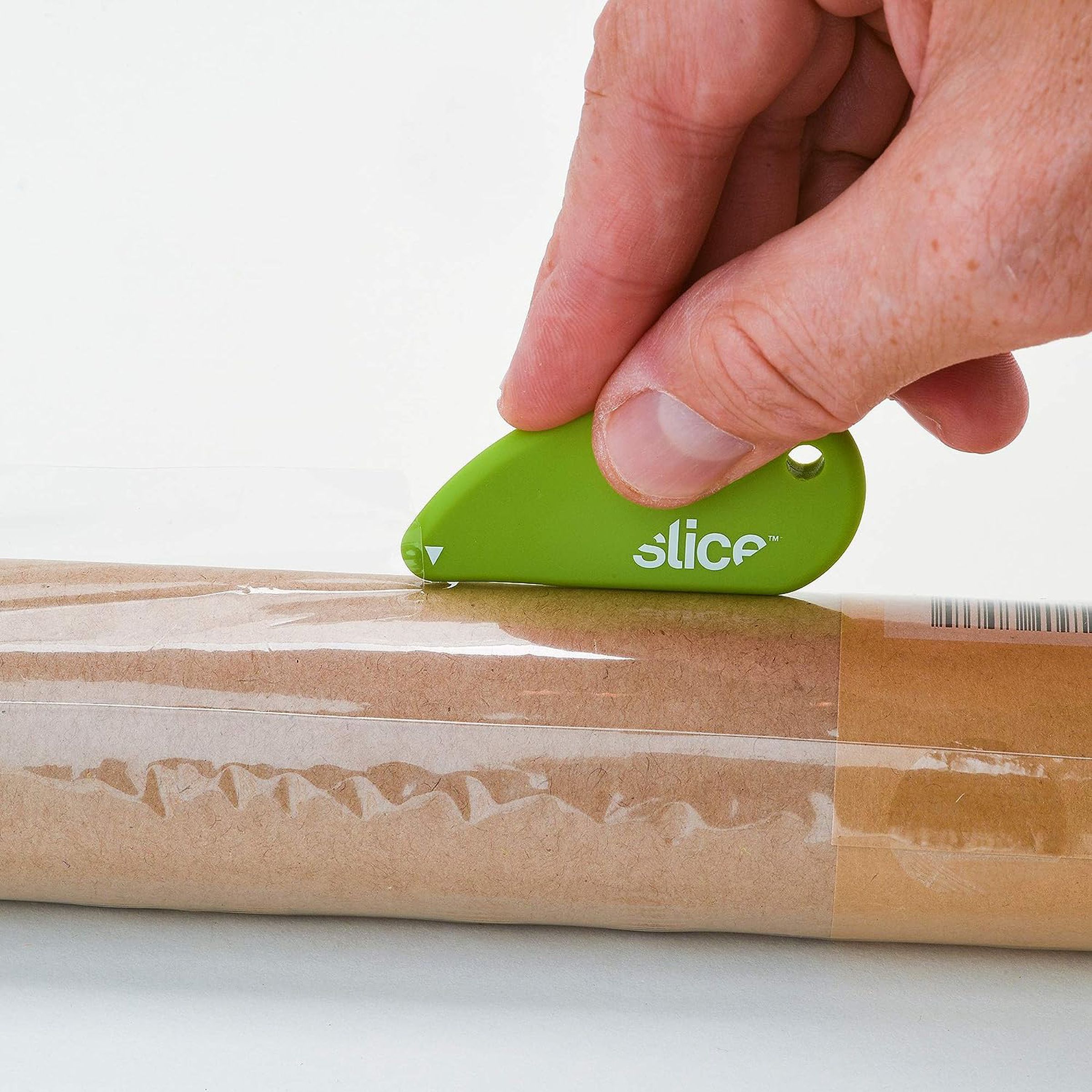 Hand holding green safety cutter over a wrapped brown tube.