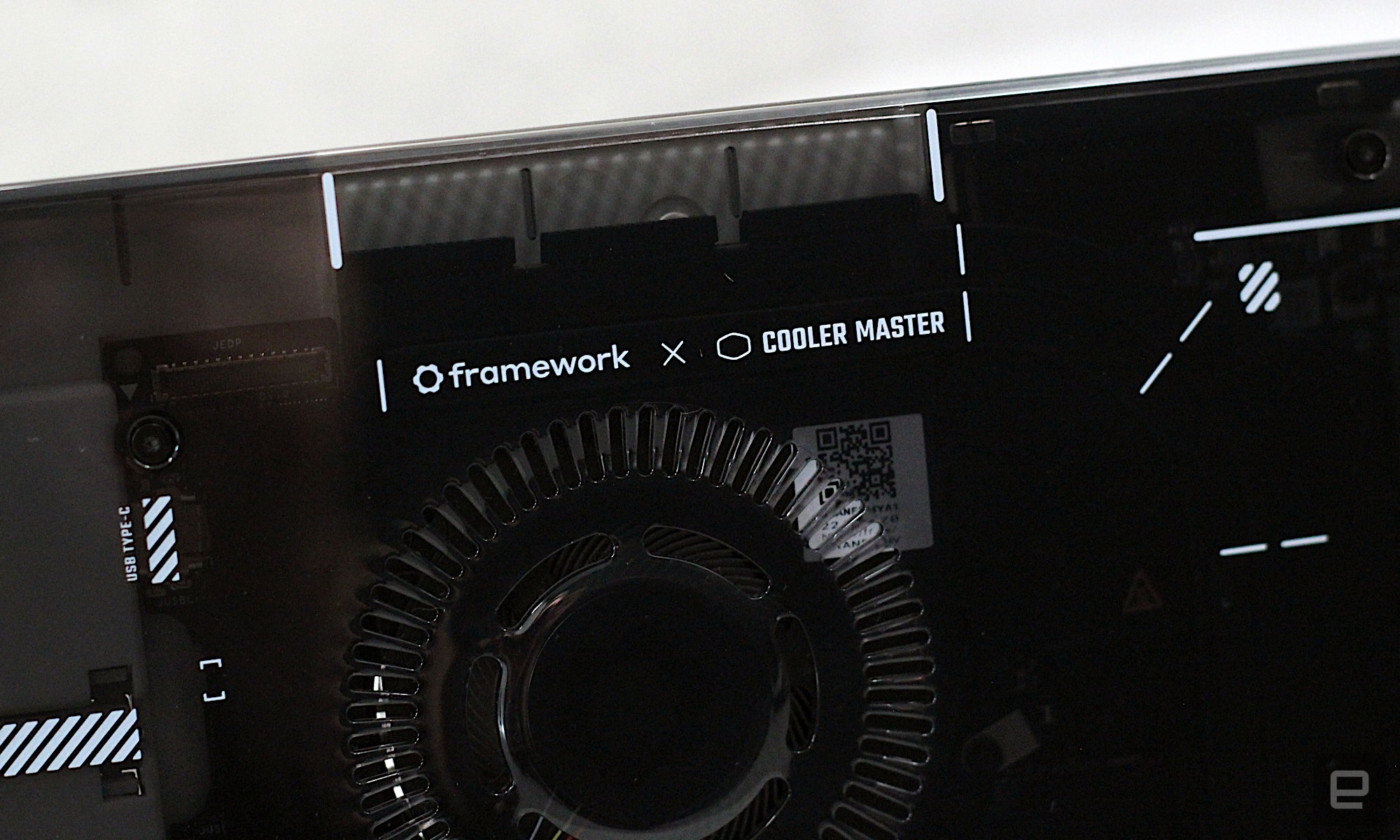 Close-up of the Framework x Cooler Master logo on the front of the case in front of a gray painted wall.
