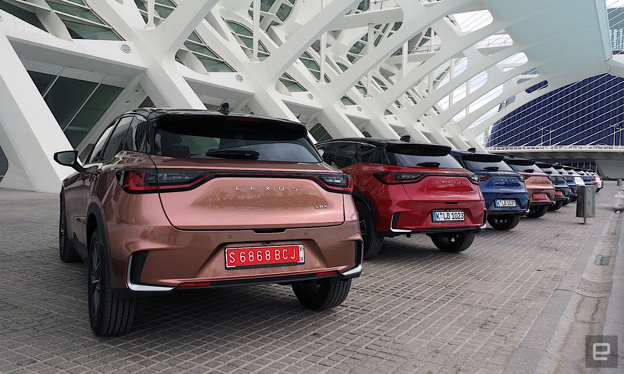 Image of a Lexus LBX parked under the marquee of the City of Arts and Sciences in Valencia.  The car is painted in “Sonic Copper”, a kind of metallic orange.