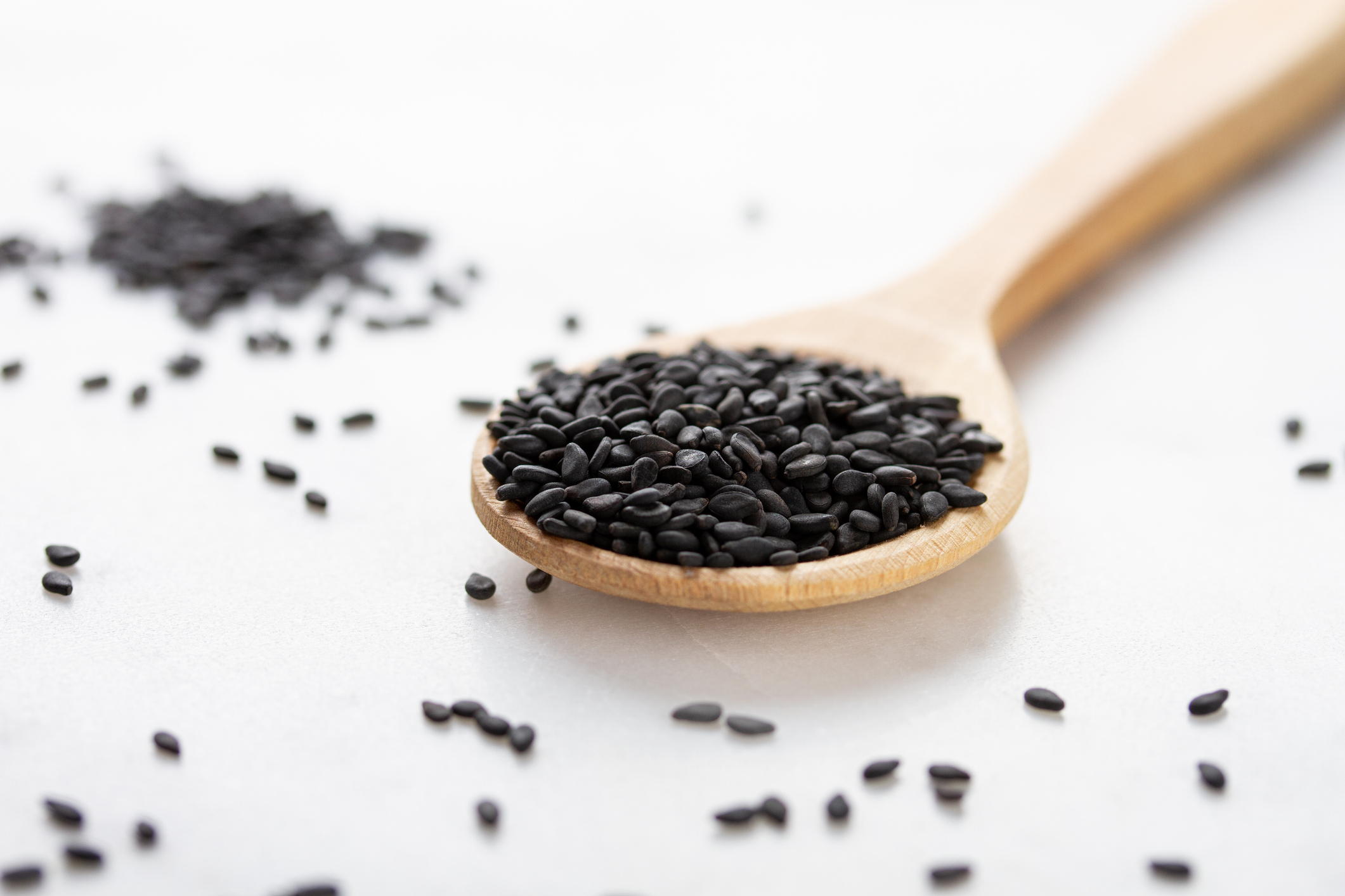 Black sesame seeds in a wooden spoon on a white background.