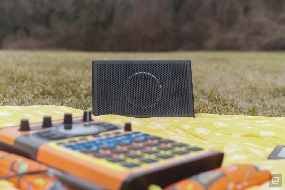 AIAIAI Unit 4 Wireless+ studio monitor on a yellow floral picnic blanket in a park with an SP-404 MKII in the foreground in that objectively dope Speak & Spell skin. Shout out to Cremacaffe.