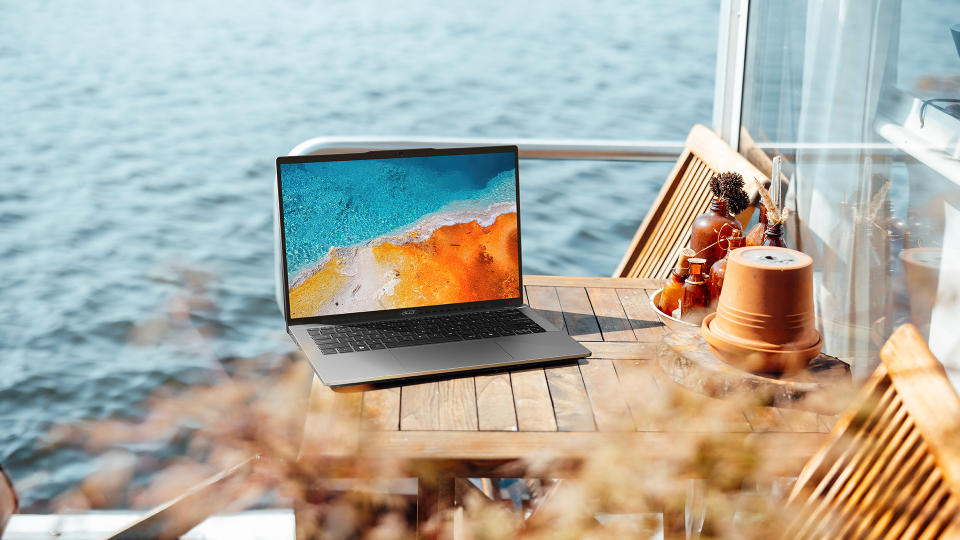 Lifestyle marketing image of the Acer Swift Go 14 sitting on an outdoor table by the beach.
