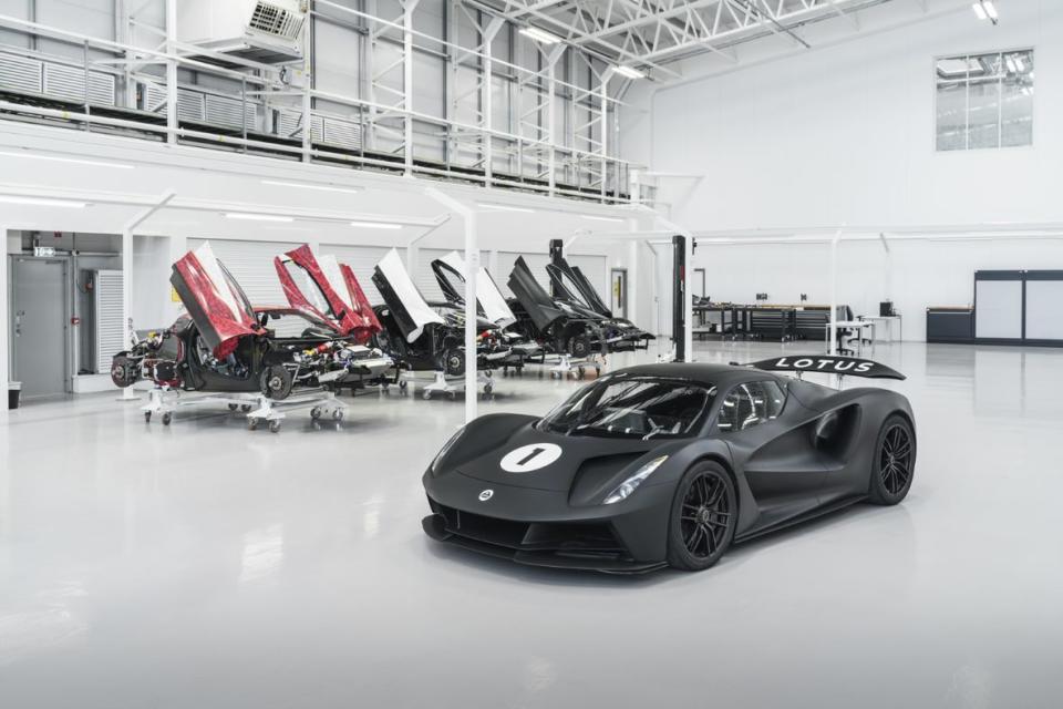 Imagen de la sala de producción de Lotus Evija con una serie de modelos a medio terminar al fondo, mientras que en primer plano se encuentra un Evija negro con librea de carreras.
