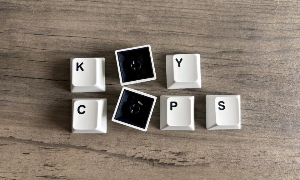 A handful of detached keyboard keycaps rest on a brown wooden table, organized in a way that spells out the words 