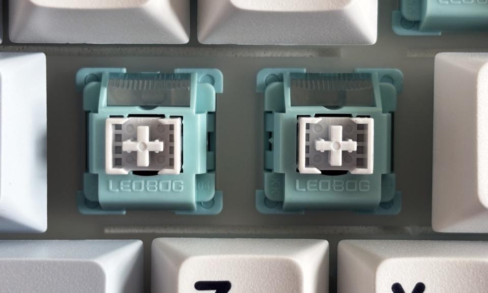 A close-up shot of a pair of exposed, white and teal mechanical keyboard switches.