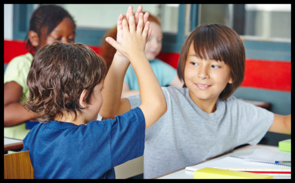 Two children in a classroom exchange high fives.