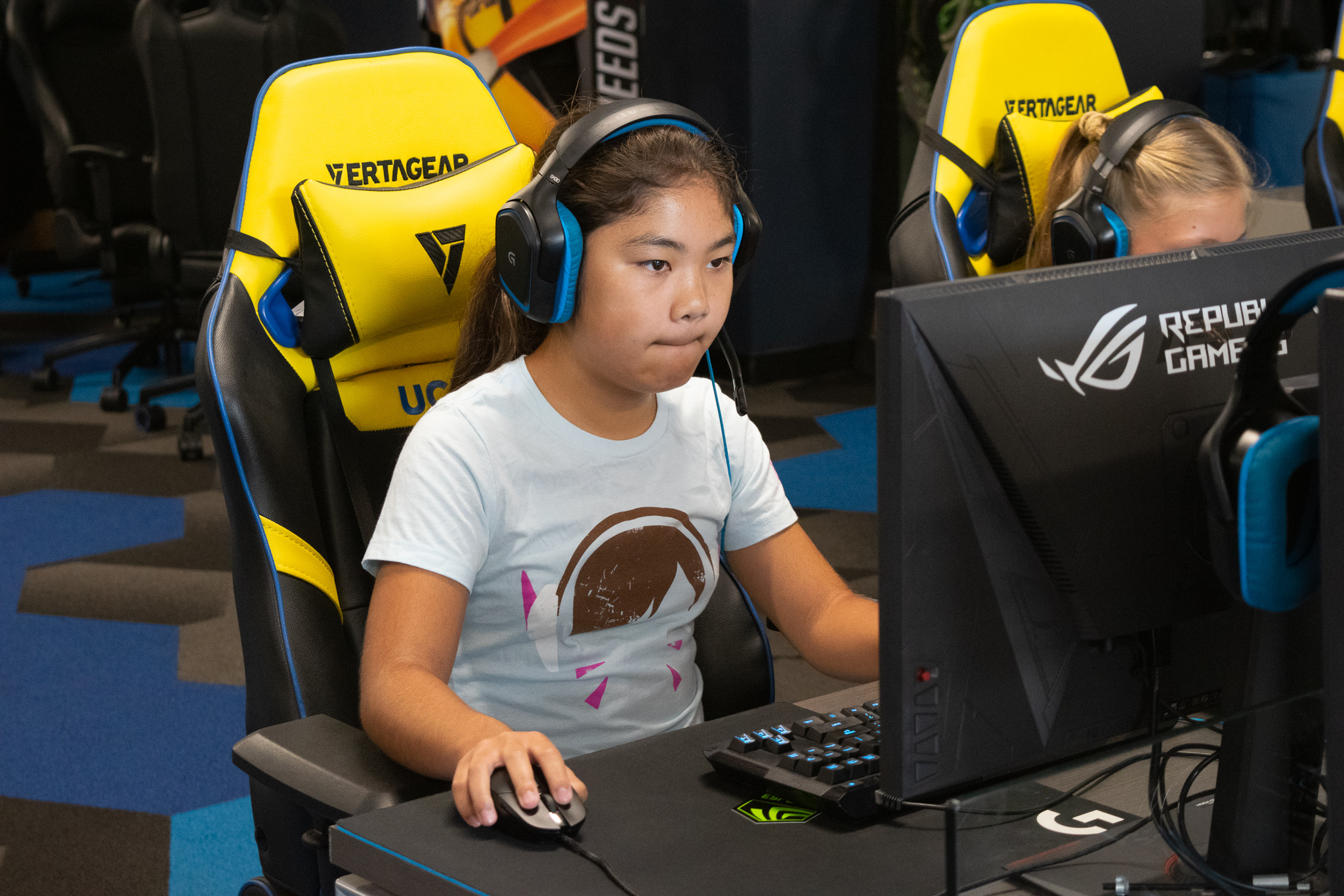 A young girl wearing headphones is sitting in front of a computer screen playing e-sports.