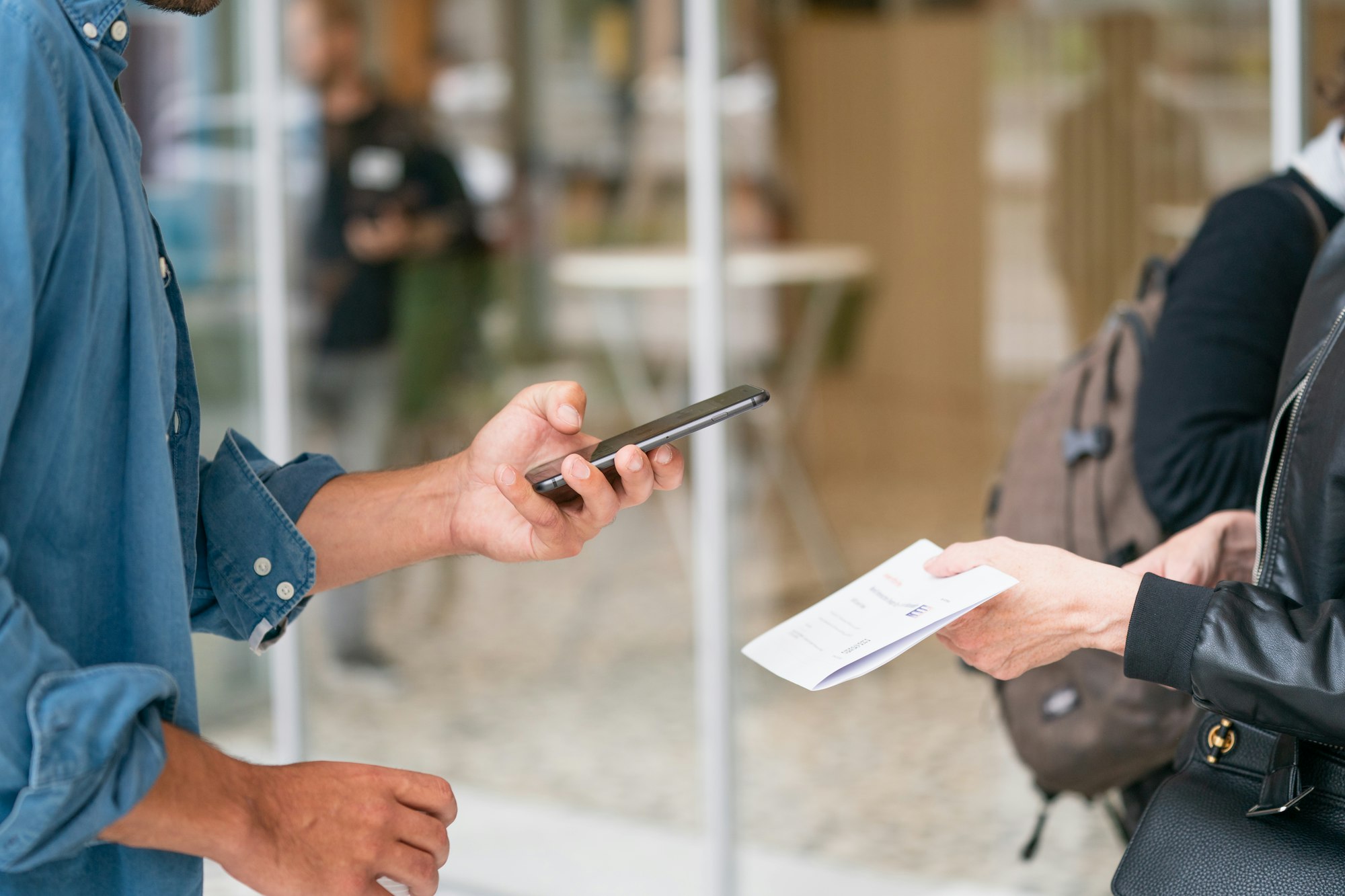 Man holding a smartphone in front of a person in a black leather jacket