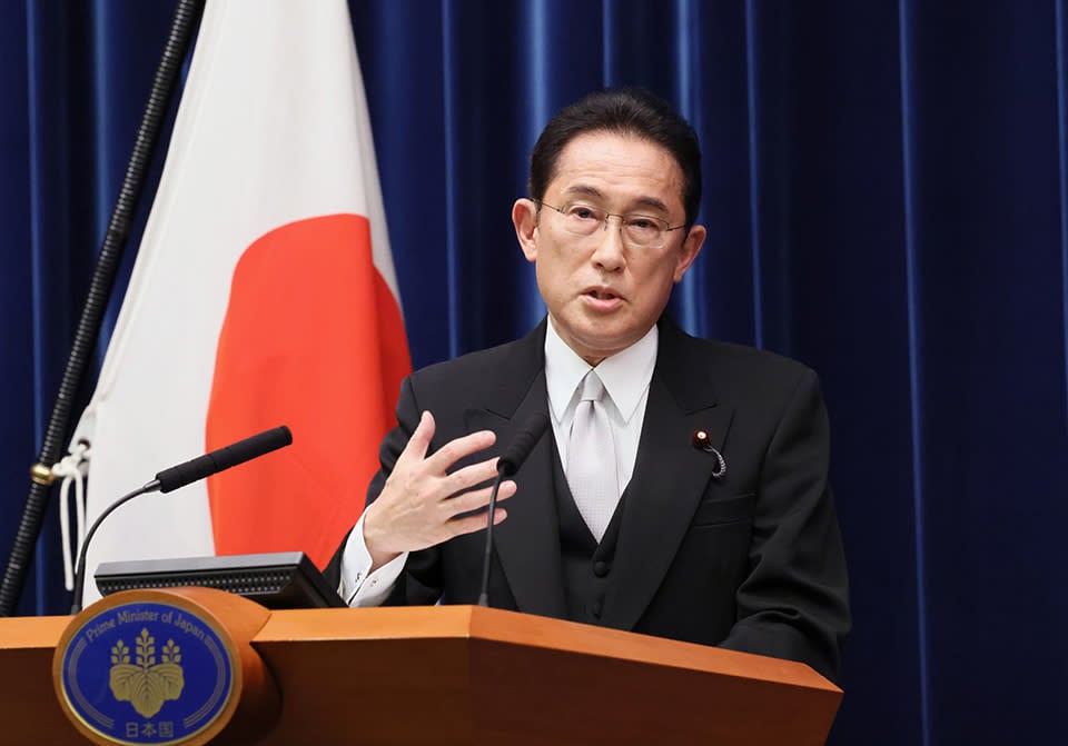 Japanese Prime Minister Fumio Kishida delivers a speech at a podium in front of the nation's flag.