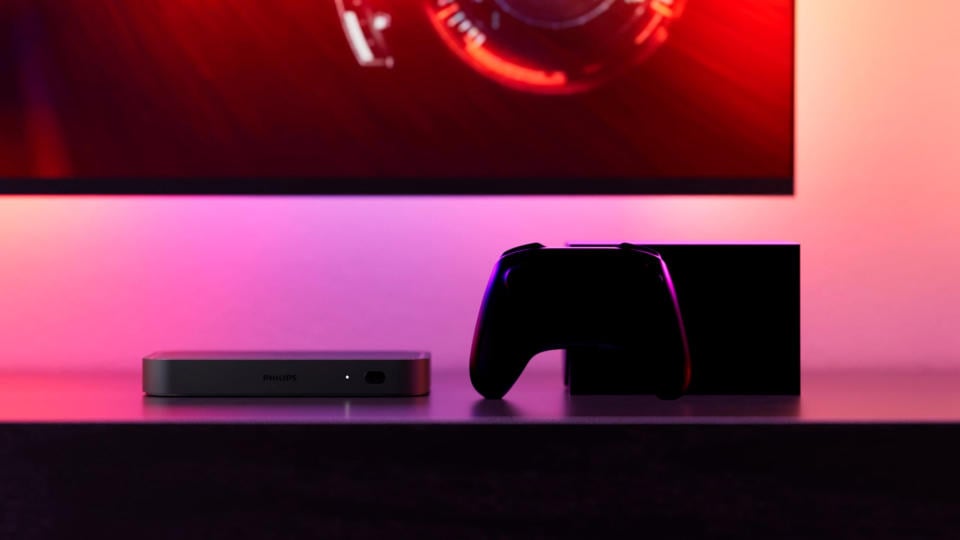 Close-up of a game controller and console (in shadows) in a colorfully lit room.