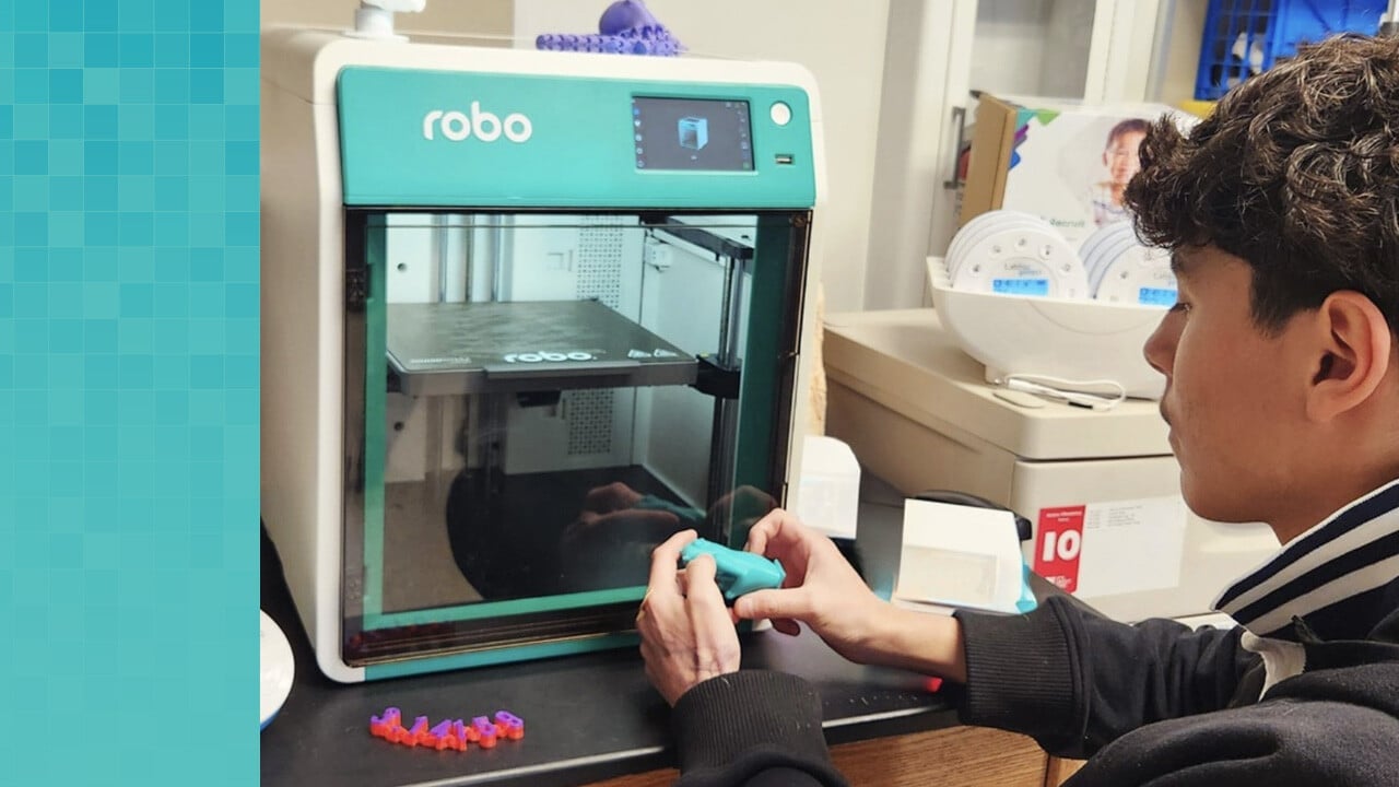 High school student holding a 3D printed ape next to a Robo 3D printer.