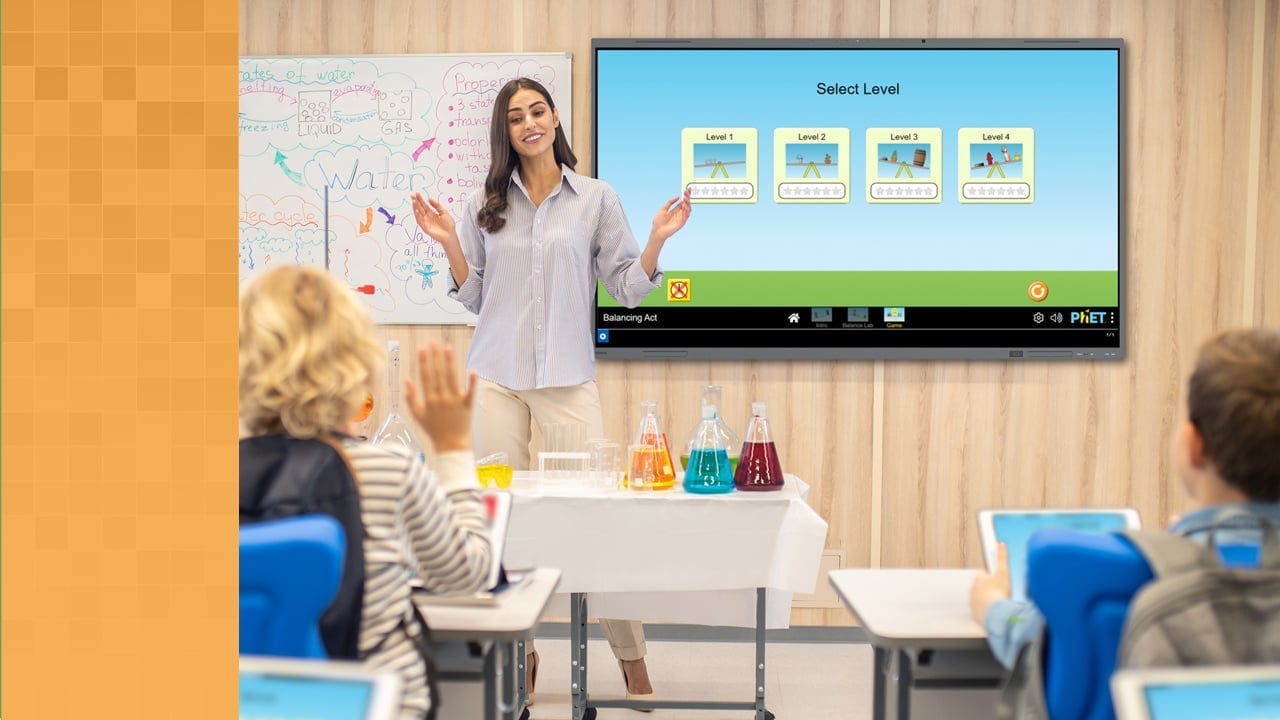 Teacher standing next to Boxlight interactive screen displaying a game available on MyClass to improve student engagement. A student with his hand raised is prepared to give an answer.