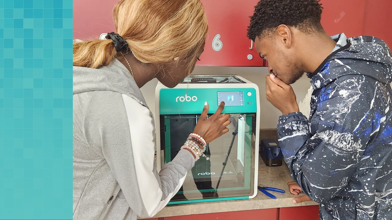 Two high school students schedule the printing of their design on the touch screen of the Robo E4 3D printer.