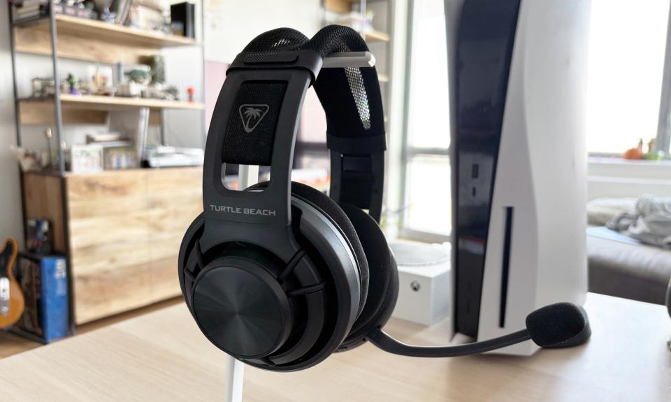 The Turtle Beach Atlas Air gaming headset rests on a stand in front of a PlayStation 5 and Xbox Series S.