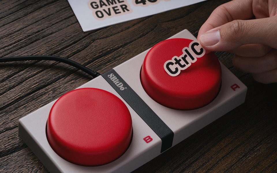 Lifestyle marketing image showing a close-up of the 8BitDo Super Buttons. A person's hand places a 