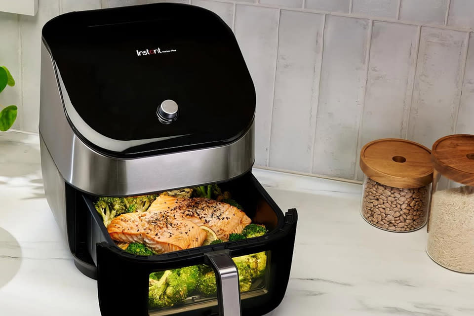 The Instant Vortex Plus air fryer sits on a counter with some retro jars of rice and beans in the background. 