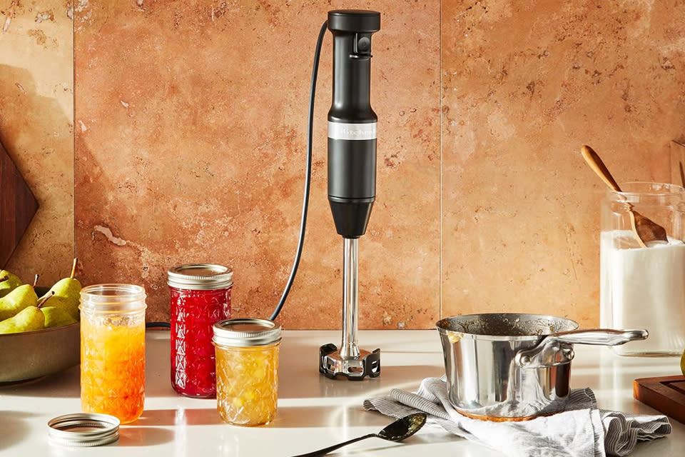 KitchenAid variable speed corded hand mixer sits on a counter with various blended foods nearby