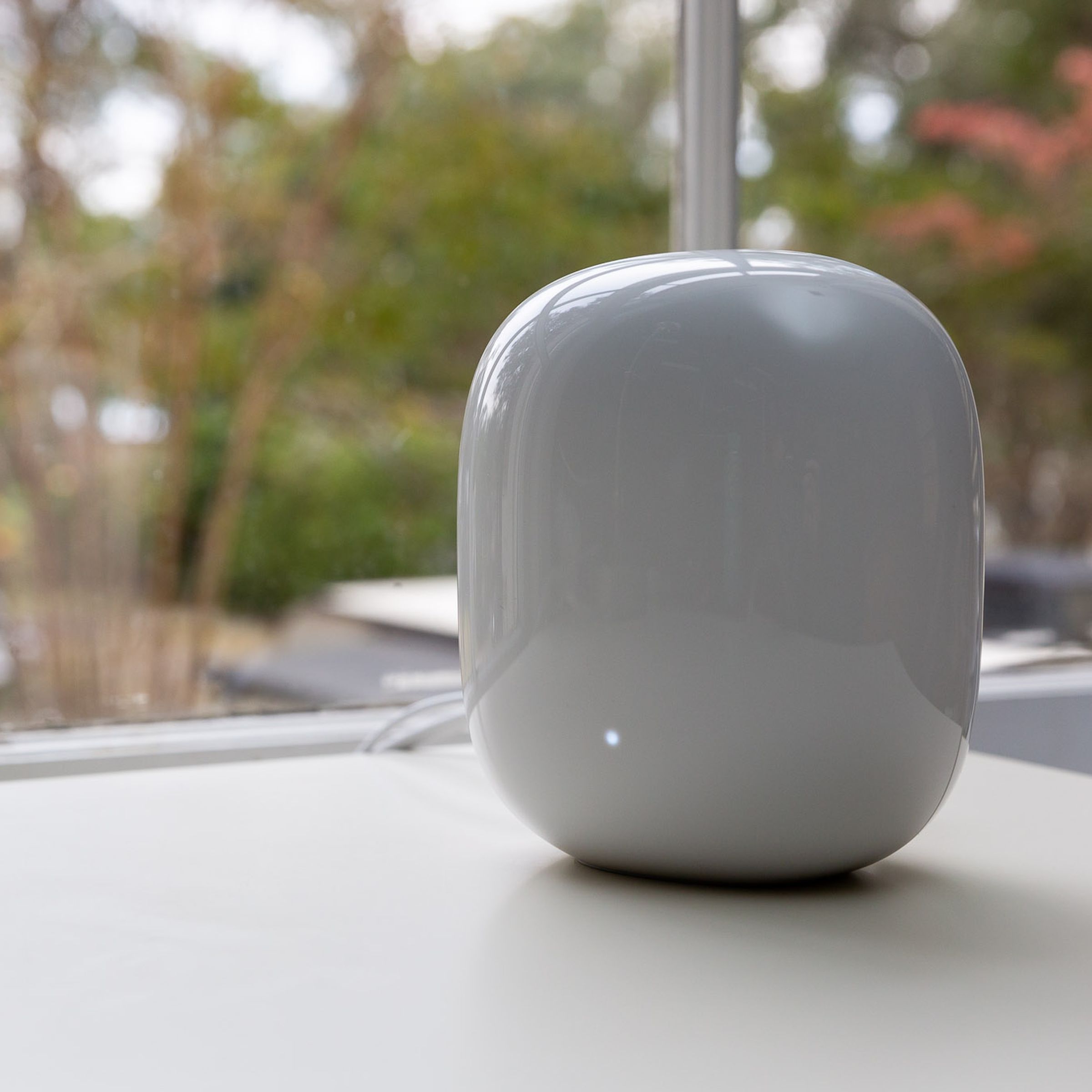 White Google Nest Wifi Pro router on a white table in front of a window.