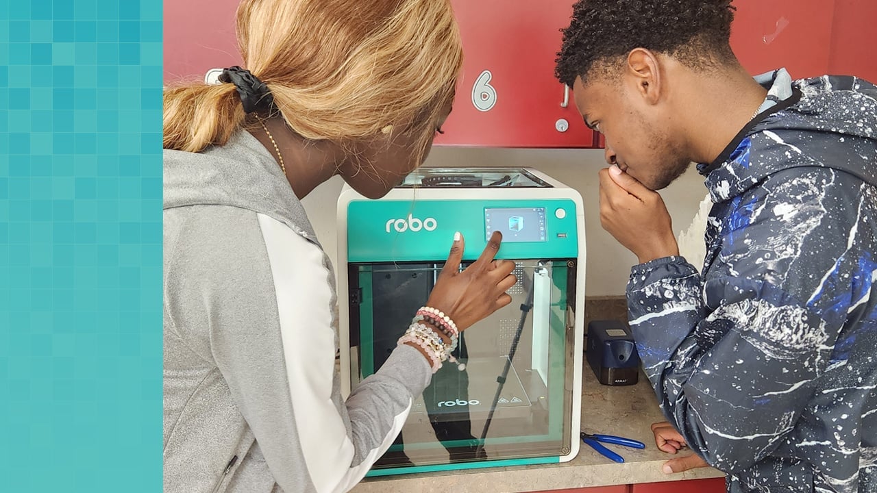 Dos estudiantes de secundaria tocando la pantalla de una impresora Robo 3D.