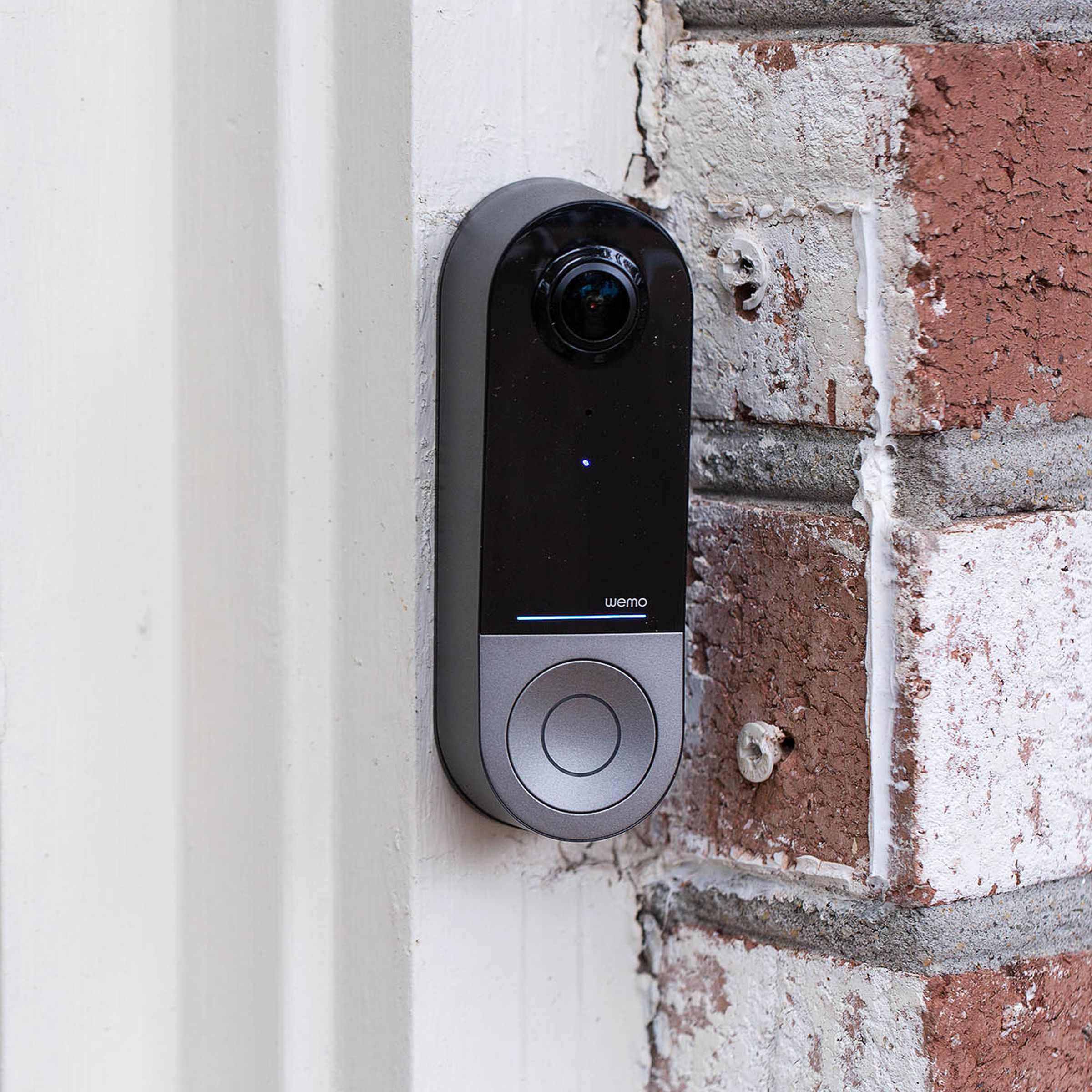 A black and silver doorbell with a camera on a brick wall.