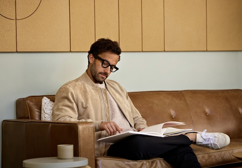 A person sitting on the couch wearing glasses while looking at a book.