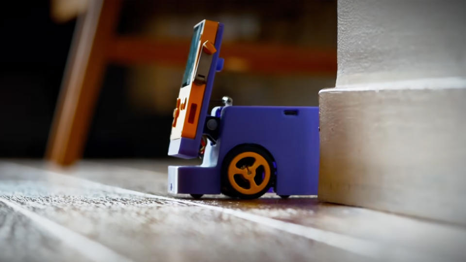 A Playdate console attached to a motorized or wheeled base, navigating around a corner of someone's home.