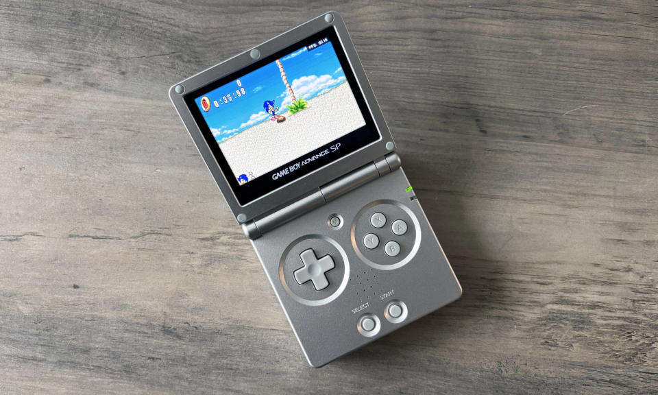 The Anbernic RG35XXSP gaming handheld rests on a brown wooden table.